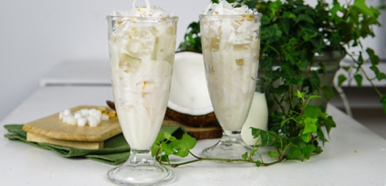 A cup of coconut dessert drink is filled with coconut milk and lots of toppings. 