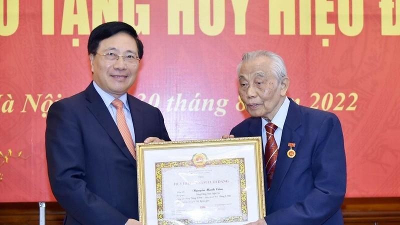 Deputy PM Pham Binh Minh presents the 75-year Party membership badge to former Deputy PM and Foreign Minister Nguyen Manh Cam. (Photo: baoquocte.vn)