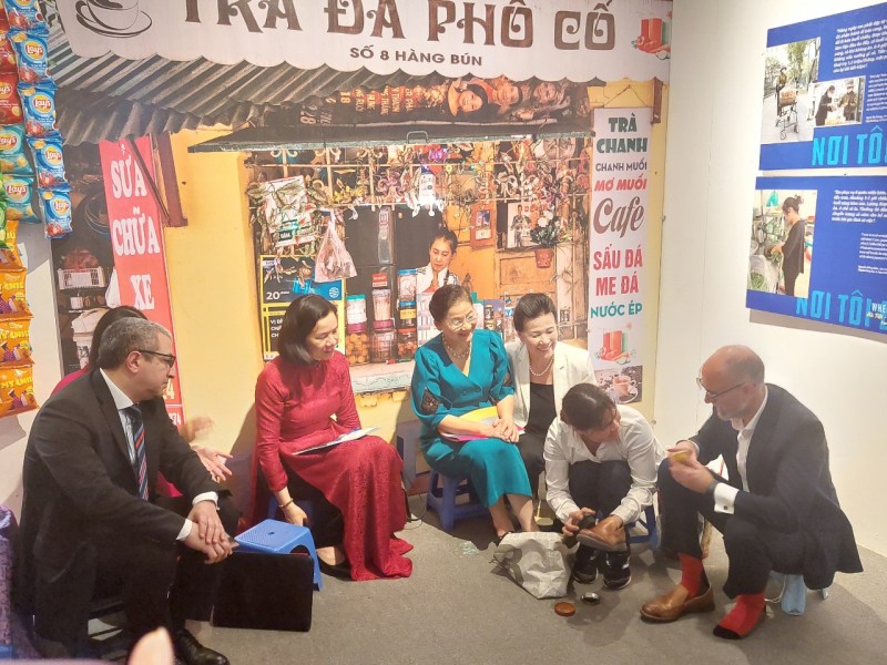 Canadian Ambassador to Vietnam Shawn Steil (first from right) gets his shoes polished by a migrant woman at the exhibition (Photo: daibieunhandan.vn)