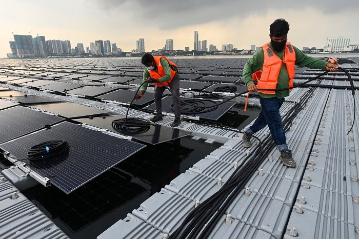 Workers laying cables on a floating solar power farm at sea, off Singapore's northern coast just across the Malaysian state of Johor (background). (Photo: AFP)
