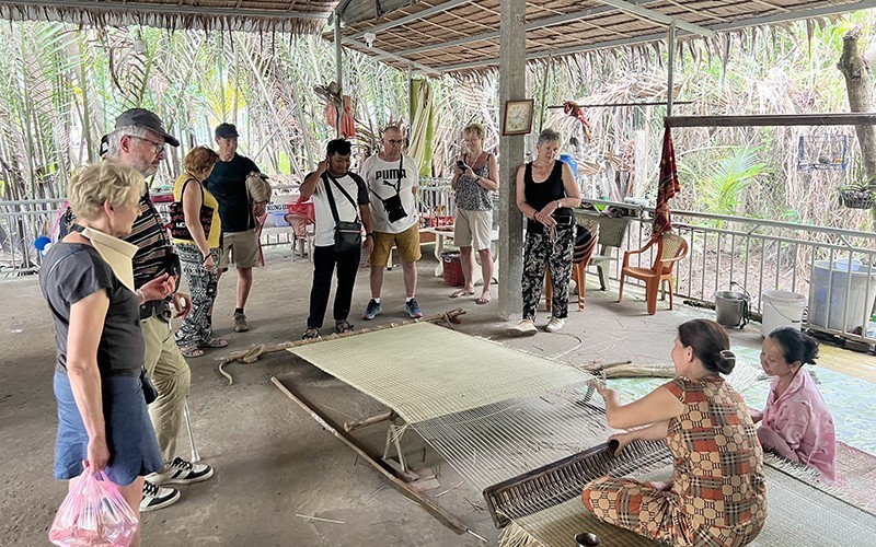 Foreign tourists watch the mat weaving process in Nhon Thanh Commune, Ben Tre City, Ben Tre Province.