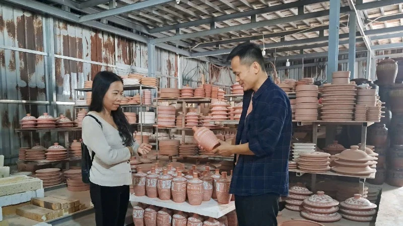 Artisan Nguyen Manh Hoa (right) introduces new products to tourists.