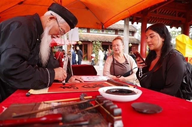 Two international tourists watch a calligrapher writing in Hanoi. (Photo: VNA)