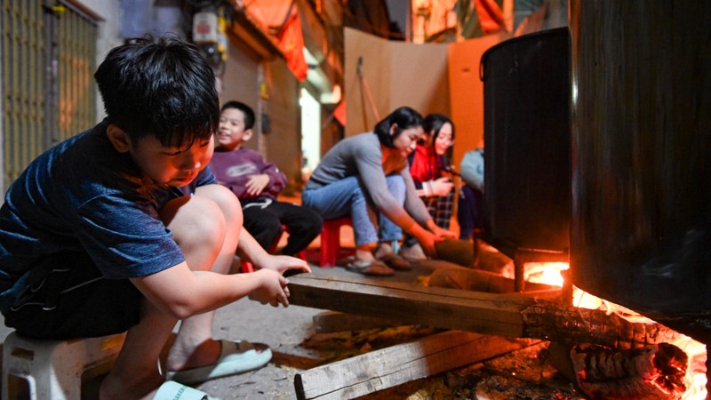 Adults and children gather and stay up all night in many alleys in Hanoi to watch over the pot of banh chung for Tet.