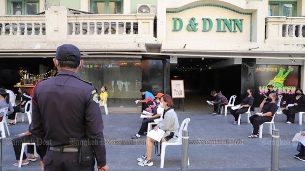 A Bangkok city "thetsakit" inspector keeps a watch on office and shop employees on Khao San Road waiting for COVID-19 tests. (Photo: Pornprom Satrabhaya via Bangkok Post)