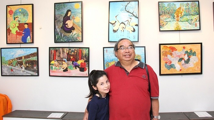 Painter Pham Trong Chanh with his paintings on display in the background at the exhibition 