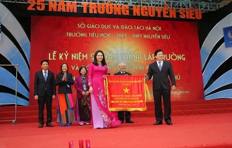 Deputy Prime Minister Trinh Dinh Dung (R) presents the emulation flag of the Government to teachers and students of Nguyen Sieu Private School.
