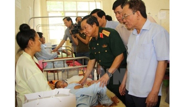 National Assembly Deputy Chairman Do Ba Ty (in military uniform) joined local leaders to visit and present gifts to Ca Van Hao, 4 years old, in Nam Pam commune, Muong La district, So La province, who was injured due to flooding on the night of August 2. (Credit: VNA)