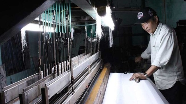 Director Tran Huu Phuong examining an old satin weaving machine (Photo: plo.vn)