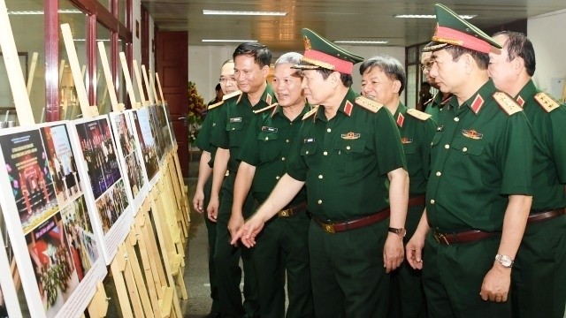 Minister of Defence General Ngo Xuan Lich (second from right) enjoys photos depicting reporters from military press agencies during their journalism operations. (Photo: NDO)