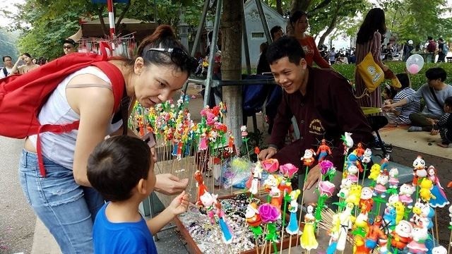 A ‘to he’ stall of artisan Dang Van Hau (L) attracts much interest from foreign visitors to the the pedestrian space around Hoan Kiem Lake (Photo: giaoduc.net.vn)