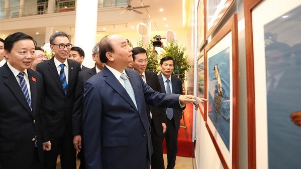 Prime Minister PM Nguyen Xuan Phuc joins other delegates to admire photos on display at the exhibition (Photo: hanoimoi.com.vn)