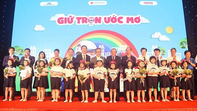 Deputy Prime Minister Truong Hoa Binh and delegates present helmets to first grade students at the launch ceremony of the "Keeping dreams" programme on July 3. (Photo: NDO/Ngan Anh)