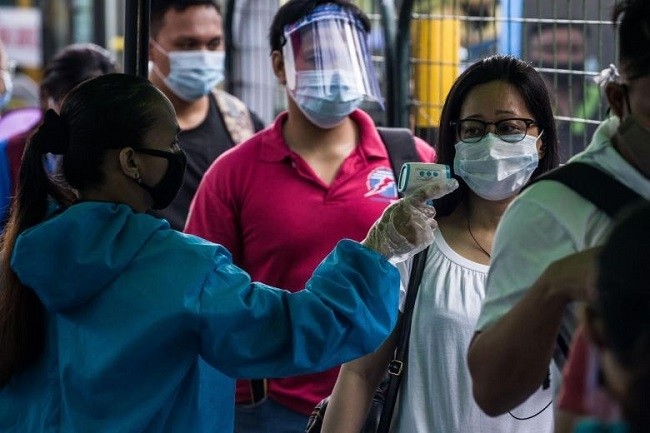 A train passenger has her body temperature taken before boarding a bus in Manila, on July 7, 2020. (Photo: AFP)