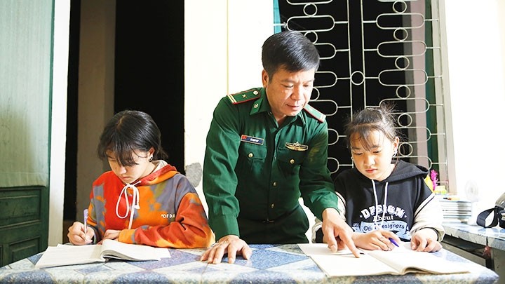 Major Le Manh Hop at the Pho Bang Border Post helps sisters Vang Thi Sau and Vang Thi Cho with their homework. 