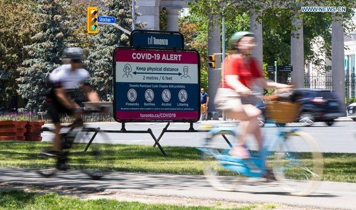 Cyclists pass a billboard reminding people to practice physical distancing in Toronto, Canada, on June 12, 2021. Canada reported 1,115 new daily cases of COVID-19 on Saturday, bringing the cumulative total to 1,400,827, including 25,910 deaths, according to CTV. (Photo: Xinhua)